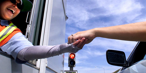 worker smiling and handing change to a car through a toll booth