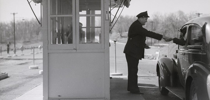old photo of a man handing change to a vehicle at a toll booth