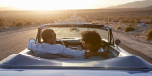 Rear view of a couple on a road trip, driving classic convertible car towards a sunset
