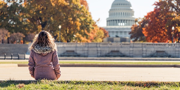 Young woman in coat sitting looking at view of United States Congress Capitol building, Washington DC