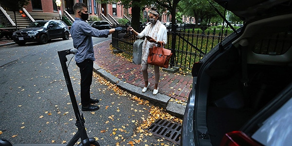 Man handing off car keys to a woman with the trunk of a vehicle open in front of them