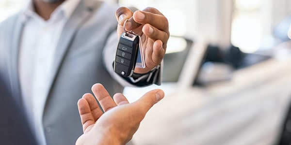 Man handing off new car keys to another person who bought the car