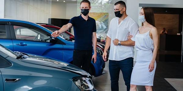 Man and woman looking at a new car at a dealership with a salesman