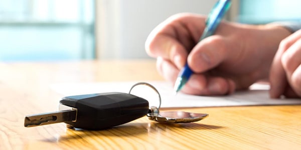 Set of keys on a table with a person writing on a paper in the background