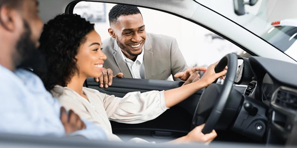 Salesman helping a couple who are sitting in a new car at a dealership