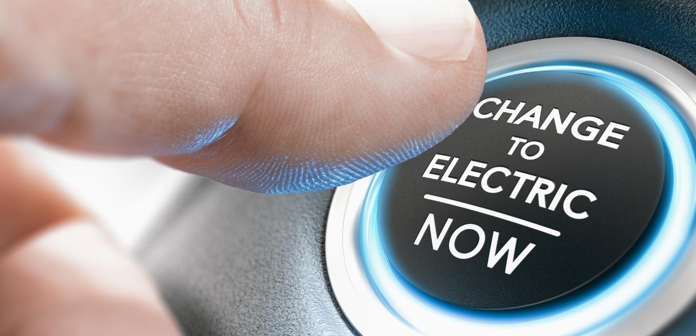 Close-up of a person pushing the ignition button of an electric car that reads: "Change to electric now"