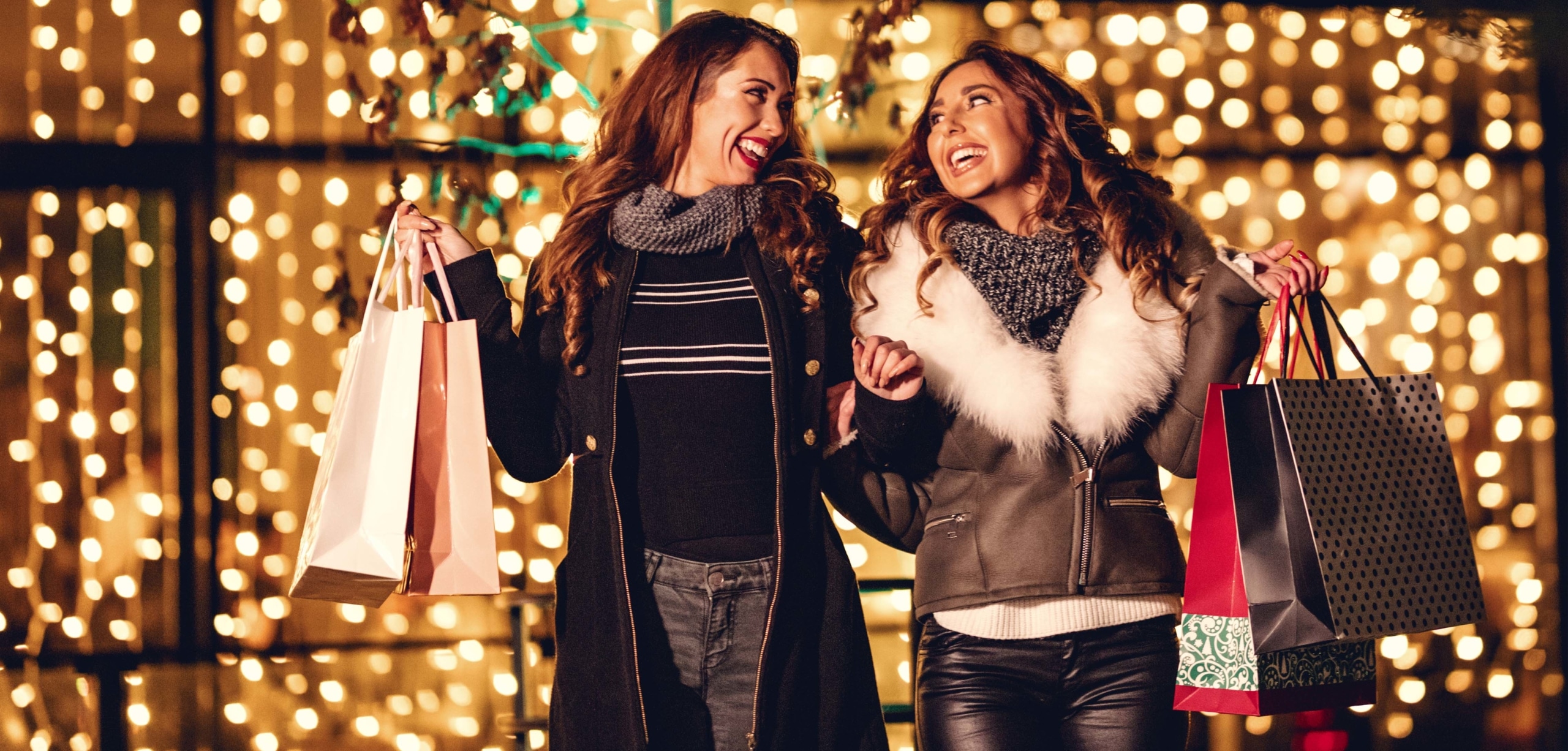 Two smiling women holding gift bags are holiday shopping | 10 Ways to Budget for the Holidays