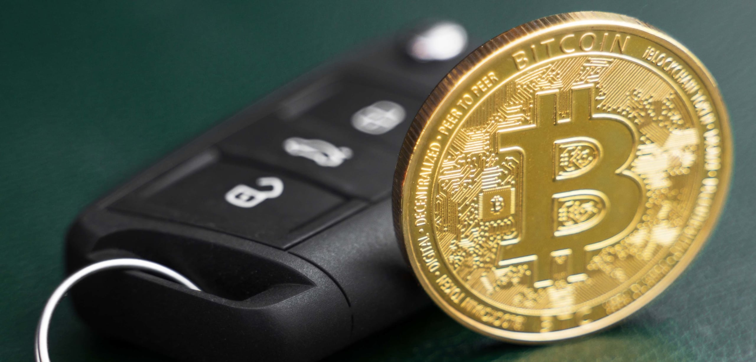 A gold token resembling a bitcoin is propped up by a vehicle key fob | Can You Buy a Car With Cryptocurrency?