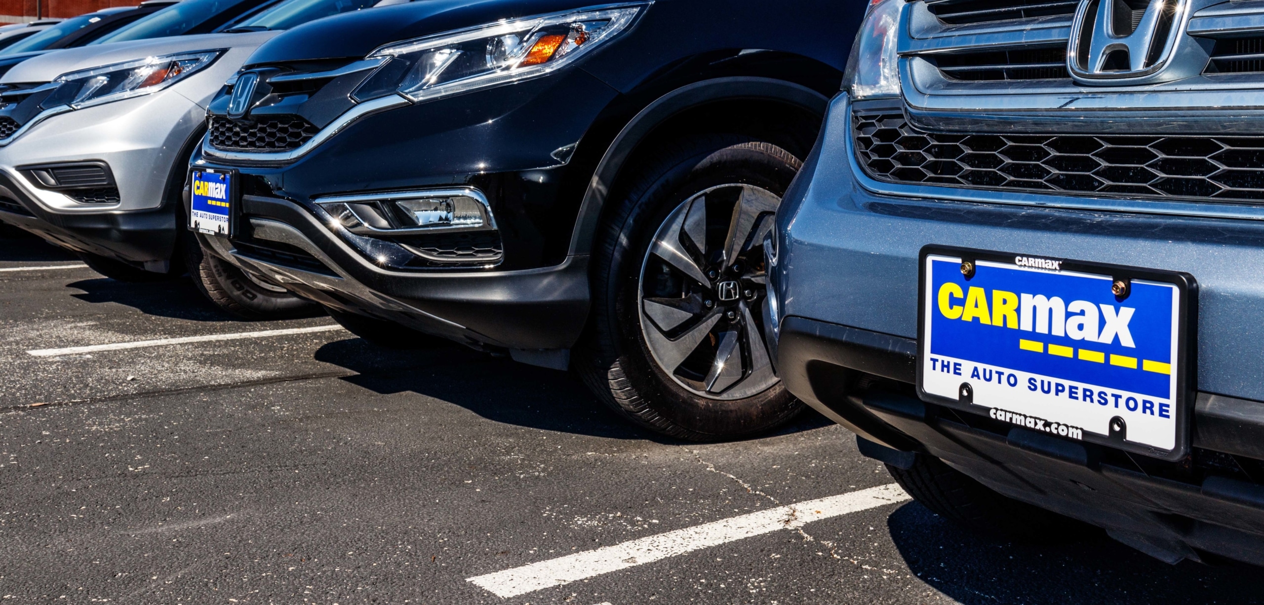 Zoomed in photo of a blue and yellow CarMax license plate on a silve Honda vehicle in a dealership lot | Should I Buy a Car From CarMax?