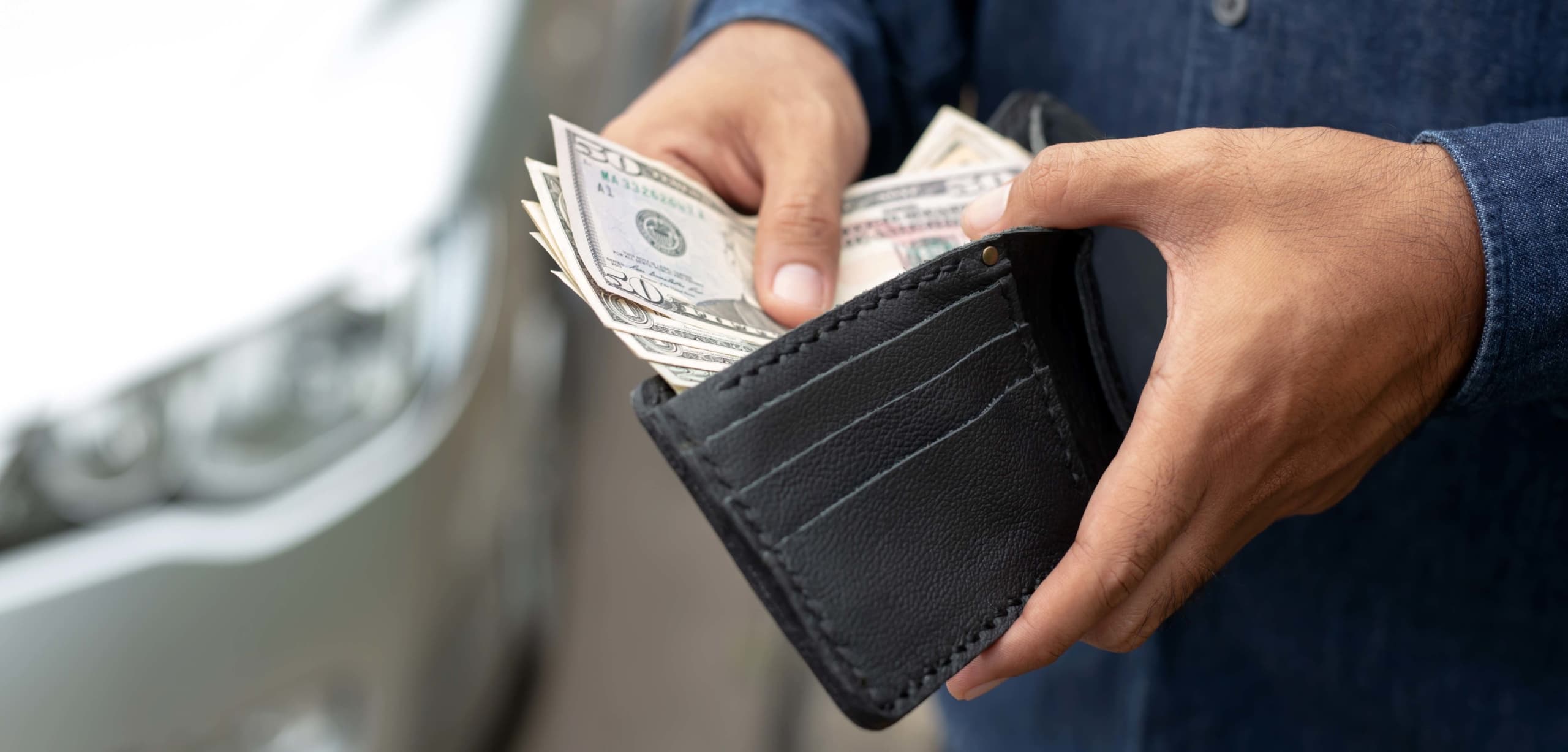 Close up of a man's hands pulling cash out of a wallet to purchase a car | Should I Pay Cash or Finance My Next Car?