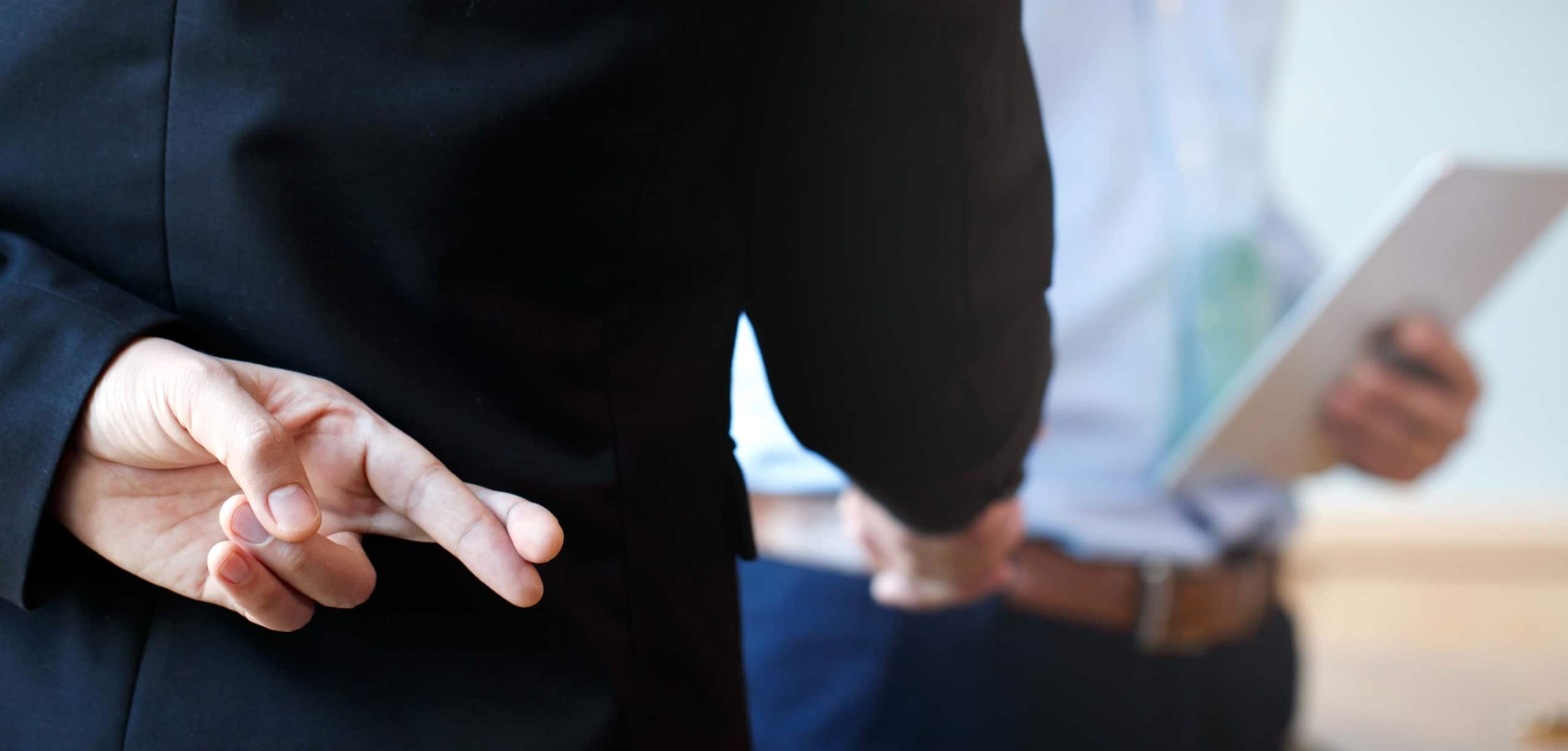 Two mean shaking hands, while the one with his back to us shows fingers crossed behind his back | 16 Car Dealership Red Flags and How To Avoid Them