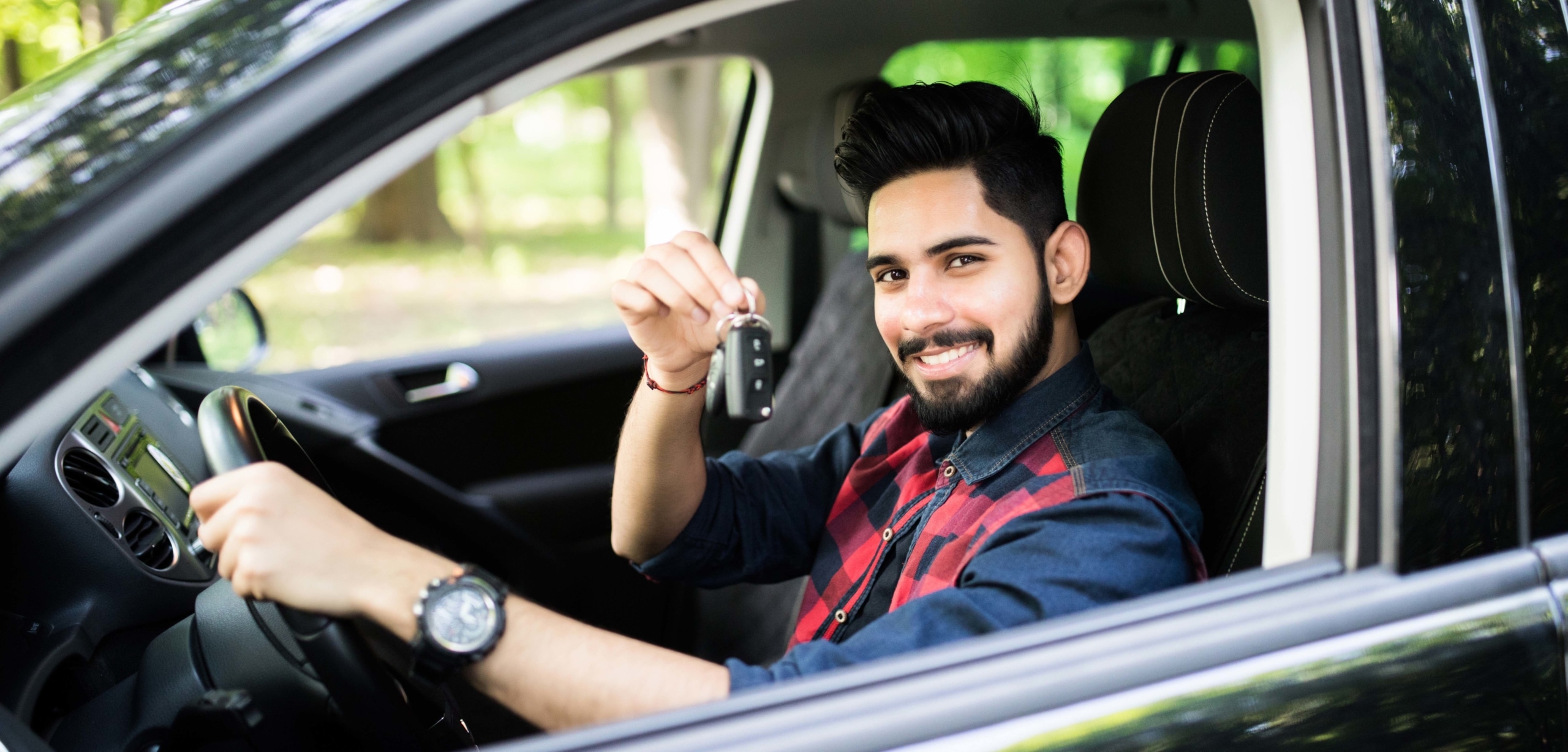 Man seated in a car holding keys and smiling at the camera | Rent-to-Own Cars: Are They a Good Idea?
