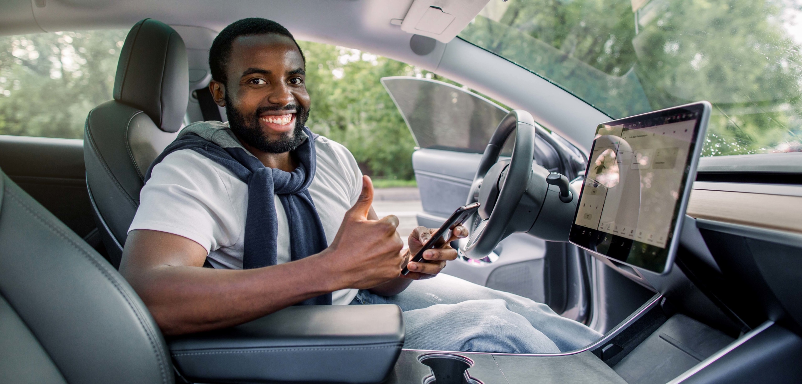 A man in the driver's seat of a car is giving a thumbs up and smiling at the camera while setting up a mounted smart screen. | Car Upgrades That Are Actually Worth It