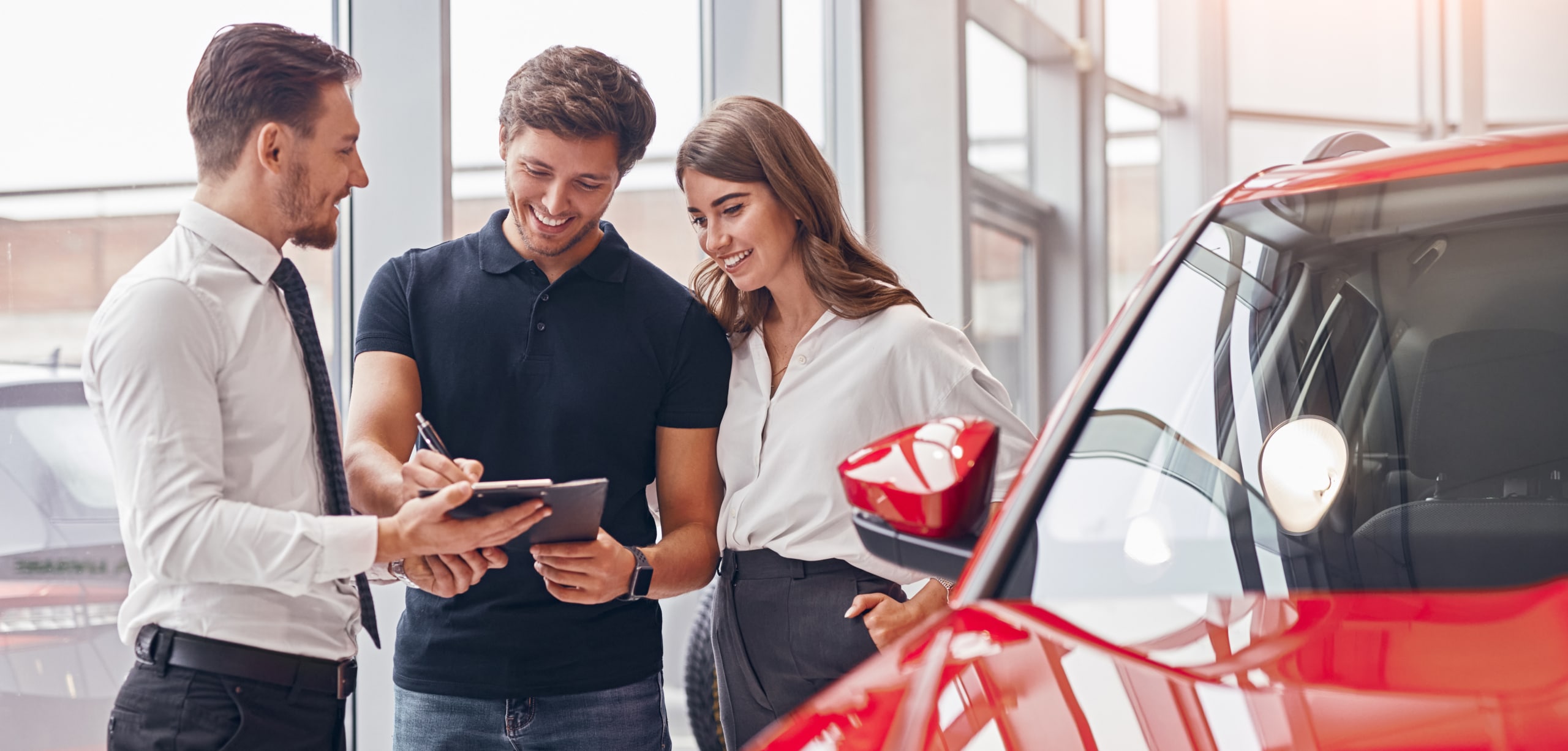 A smiling couple is signing papers with a salesperson at a car dealership | Negotiate Your Car Lease Like a Pro
