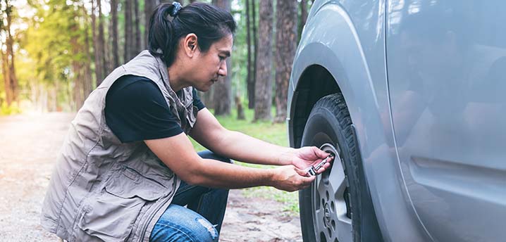 A middle aged Asian check his tire pressure on a scenic road in the forest. | Car Tire Pressure Guide