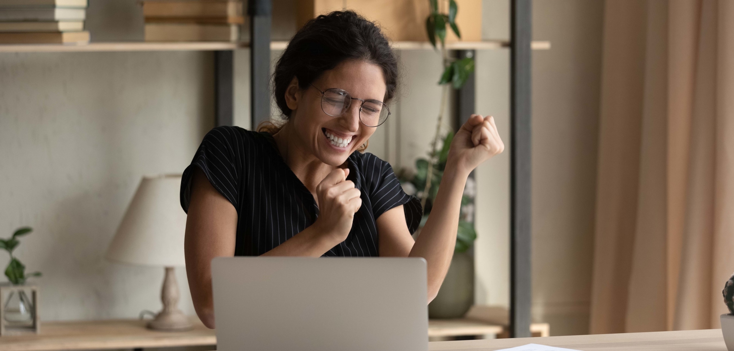 A Hispanic woman wearing glasses is excitedly dancing in front of her computer | Do I Need Good Credit To Refinance My Car?
