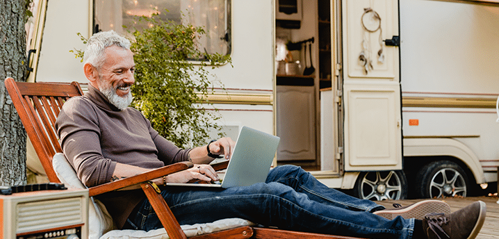 Older man smiling while working on a lap top in front of an RV | Should I Take a Remote Work Trip?