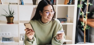 Happy, young female student holding credit card while on her phone