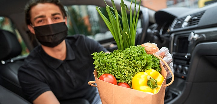 Man sitting in a car holding a bag of fresh produce to be delivered