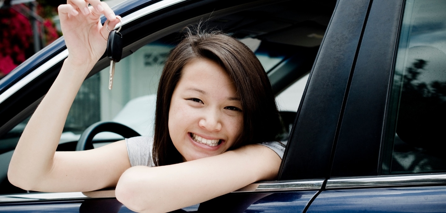 Smiling woman leaning outside car window and holding car keys