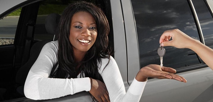 Woman leaning out of the drivers side window, accepting a car key to her new car