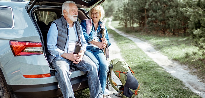 Senior couple sitting at the car trunk, enjoying nature while traveling