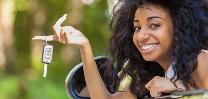 Teenage girl smiling while leaning out of a car window holding car keys