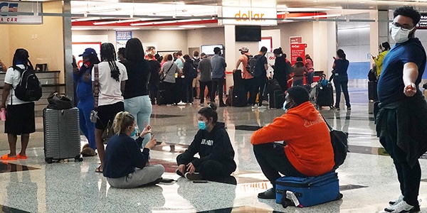 Various people waiting in line at an airport while wearing masks for COVID