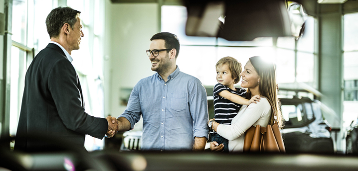 car dealership salesman and family with new car after financing