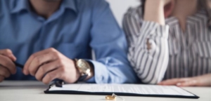 couple sitting with a divorce contract and their rings on the table in front of them