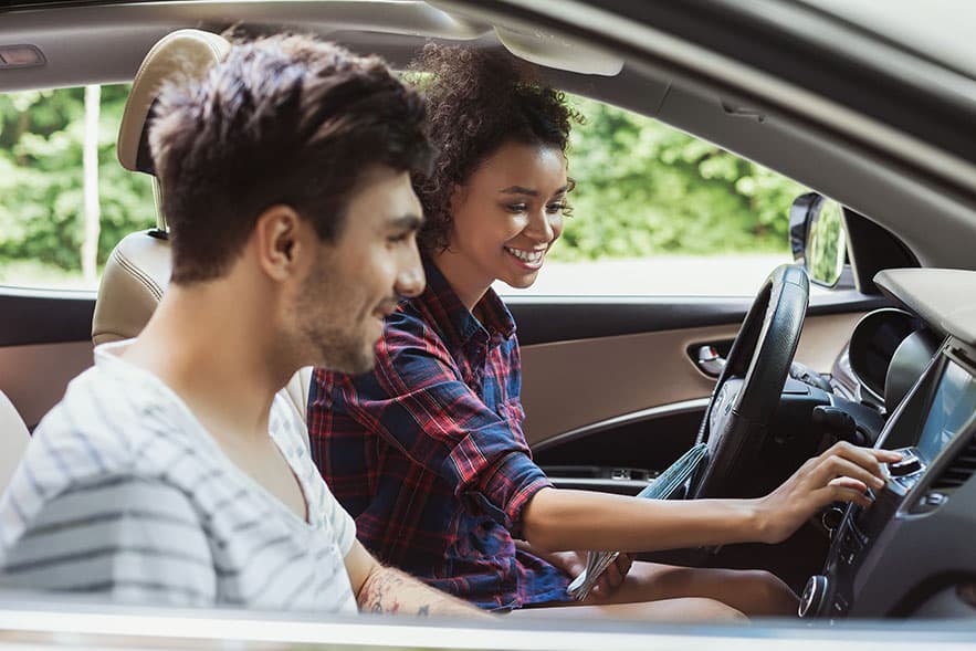 Woman driving who is looking at the dashboard and adjusting a dial while the male passenger looks in the same direction