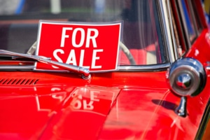 Car parked with a for sale sign on the front windshield, under the windshield wiper