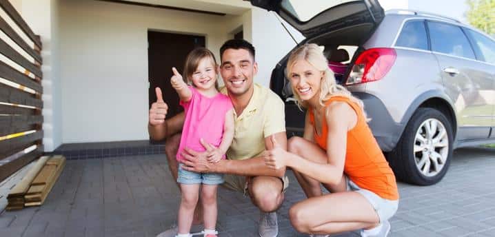 happy family kneeling in front of car while giving thumbs-up
