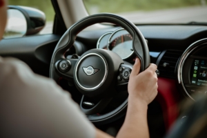 Interior of Mini Cooper car with hands on wheel.