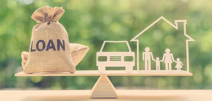 wooden scale with Loan bags of money on one side and a car and home on the other side