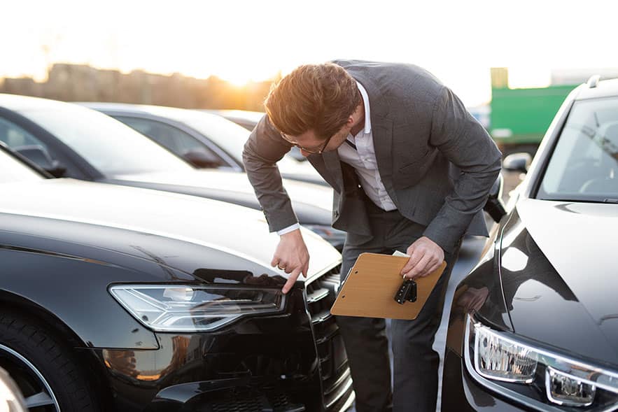 Car dealer bending down to inspect the front fender of a car