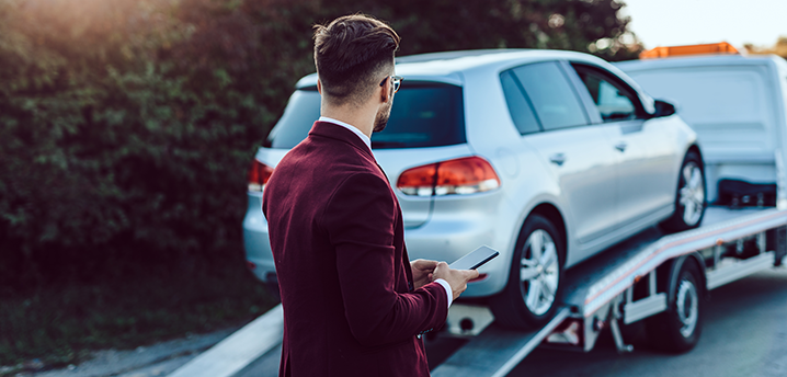 man looking at repossessed car on tow truck