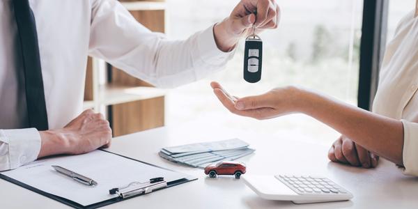 man at a car dealership handing new car keys off to a buyer