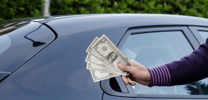 person holding money out in front of a car