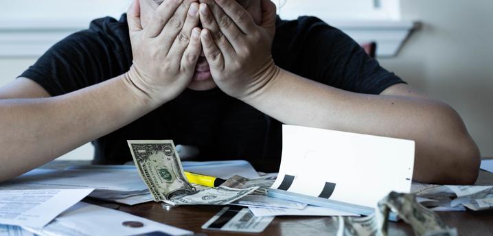 person who is stressed with hands over there face, and money and checks scattered in front of them