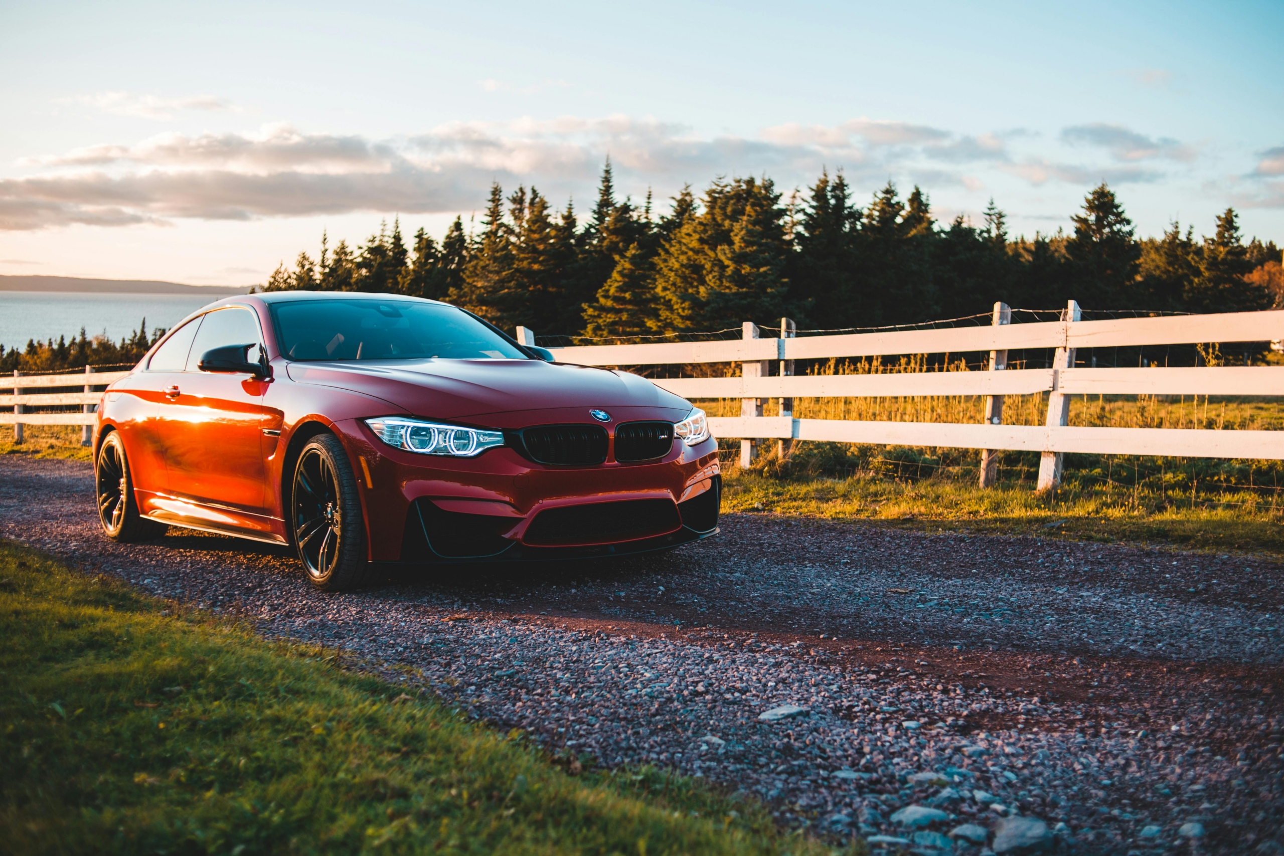 Red car in front of white fence.