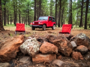 Red Jeep in forest with camping chairs.