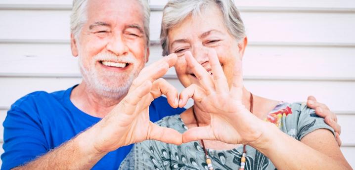 Senior couple smiling and making a heart shape using their hands