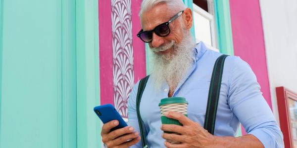 Senior man using his phone and smiling while also holding a coffee