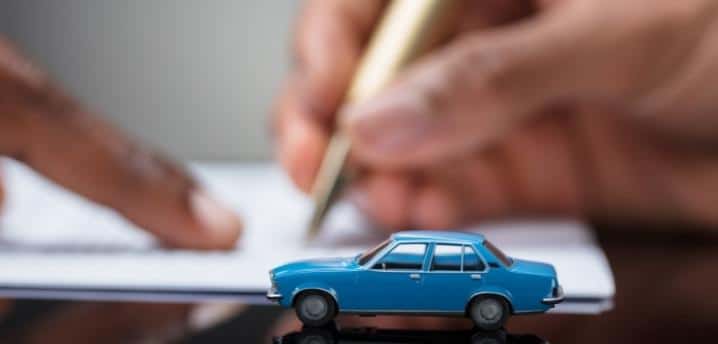 close-up of someone signing for a car loan, with a small toy car in the foreground