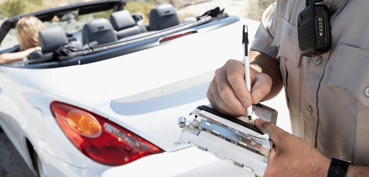 close-up of a cop writing a ticket for a white convertible car in the background