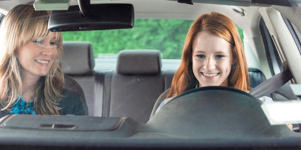 Teenager smiling while driving with her parent in the passenger seat