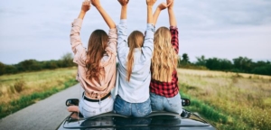 Three teenager girls sitting on the top of a convertible with their hands in the air and facing away from the camera