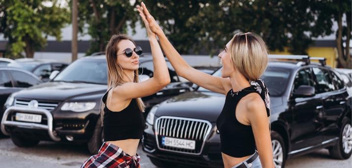 Two women high fiving in a parking lot with cars