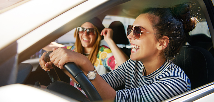 two young women driving and laughing- how to save money on car insurance